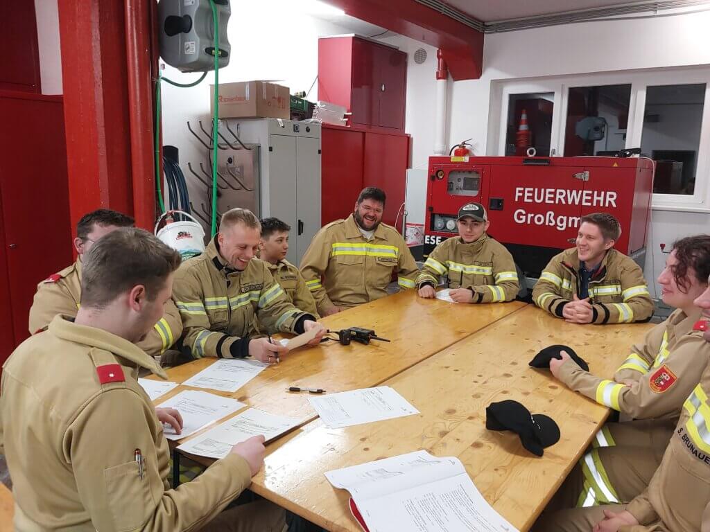 Feuerwehrleute bei einer Besprechung im Gerätehaus mit Unterlagen und Ausrüstung.