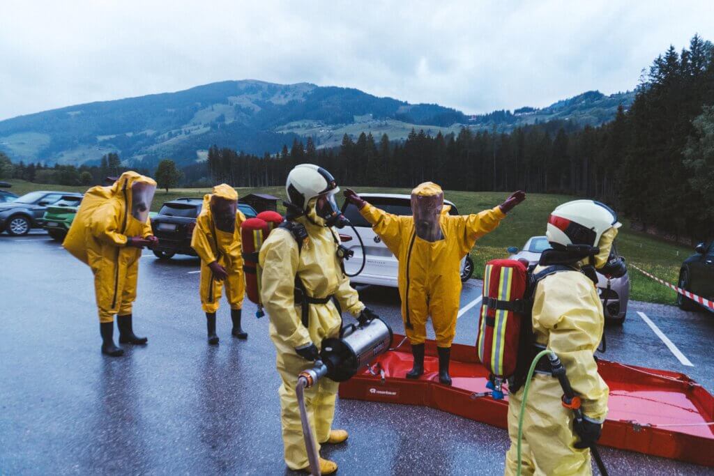 Feuerwehrkräfte in Schutzanzügen bei Übung im Freien mit Bergen im Hintergrund